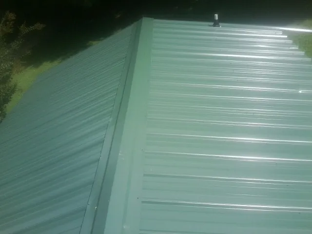 New green metal panels meeting at the ridge of a roof — Flat Roof Repair work by our crew in Cologne