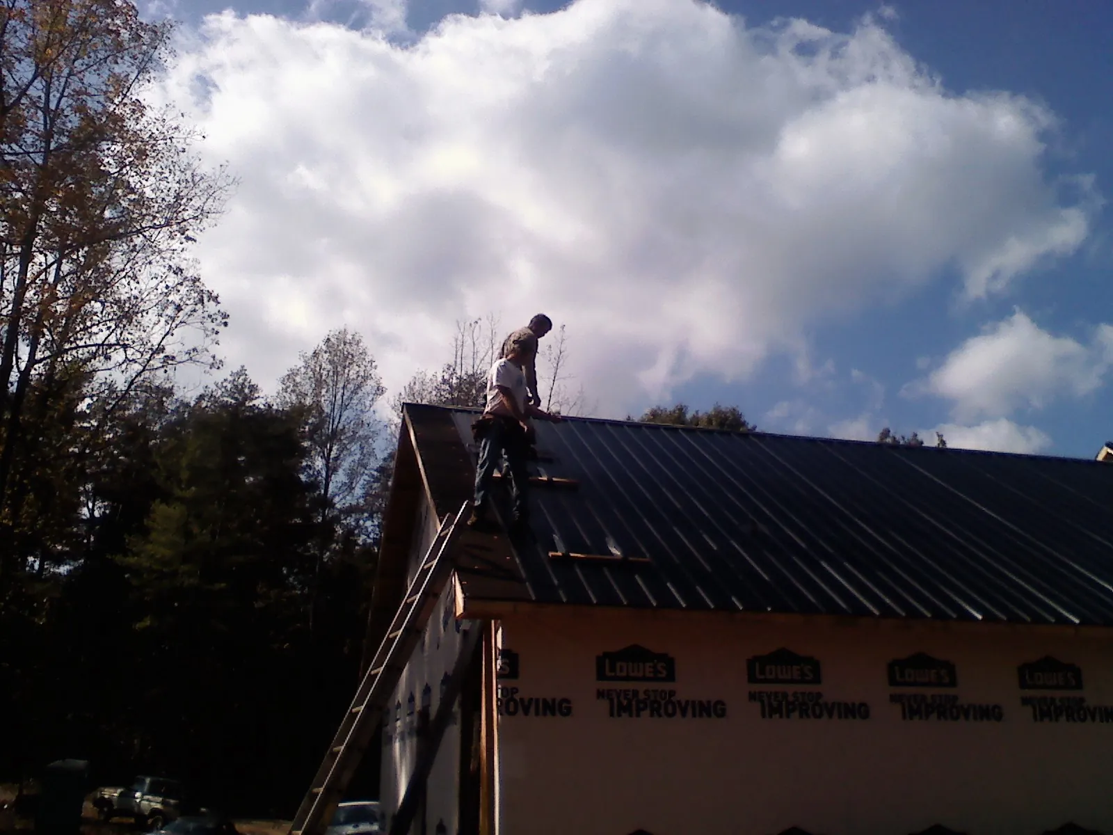 Roofer fastening dark metal panels high against a cloudy sky, from a Roof Inspection job in Cologne